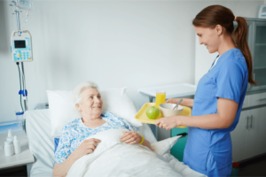 a nurse serving food to a woman in a hospital bed. Catering Assistant serving food to a woman in a hospital bed 3Q Recruitment.