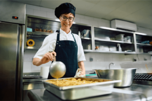 Hospital Chef - Dublin 7 3 Hospital Chef in a black apron and hat pouring liquid into a pan of food in kitchen, 3Q Recruitment