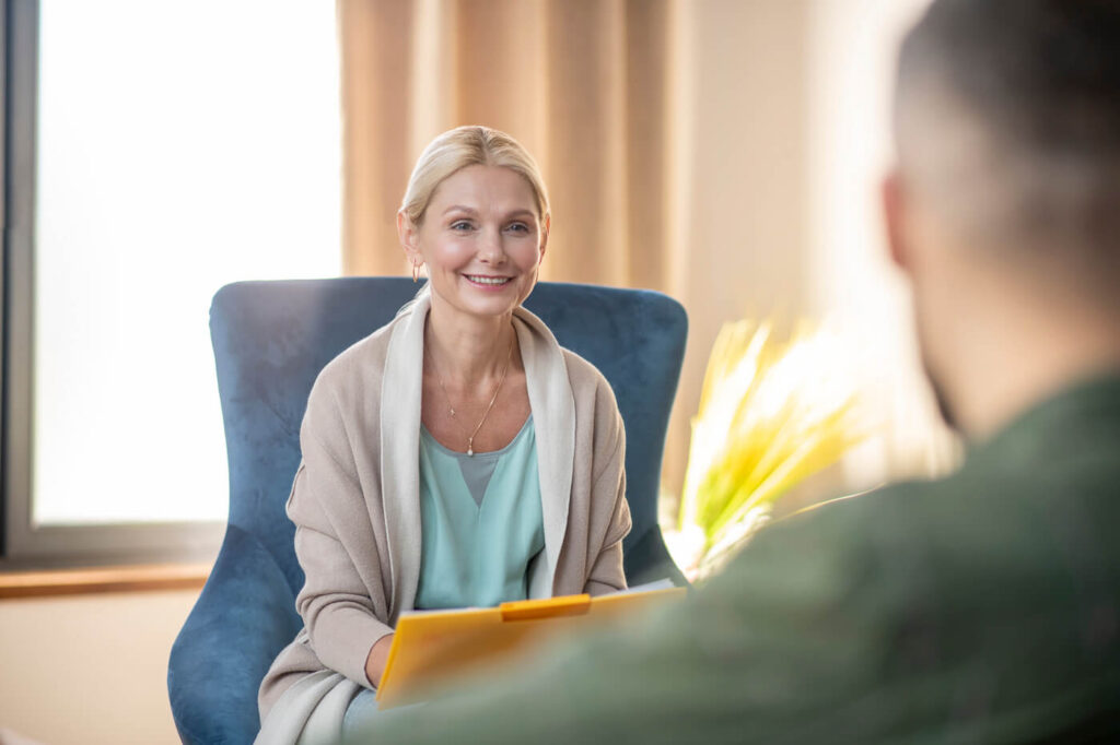 a woman sitting in a chair smiling. Social and Community Care Worker 3Q Recruitment.